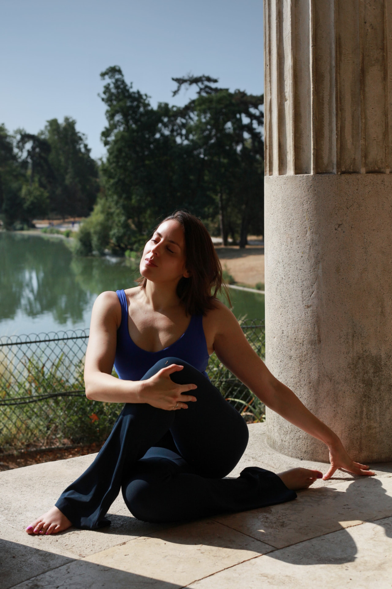Yasmine en torsion assise, à l'ombre d'une colonne, au bord de l'eau